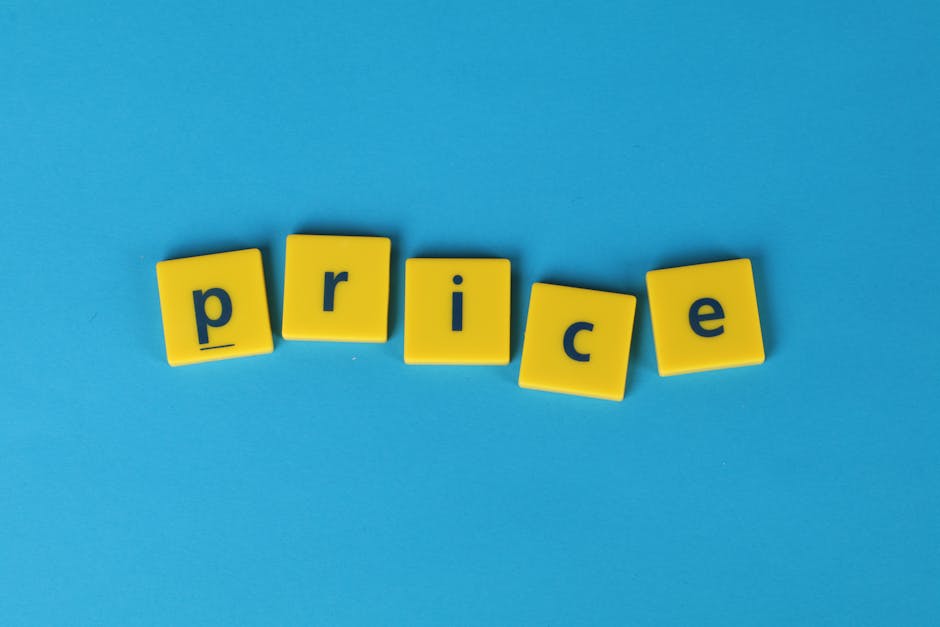 The image displays the word 'price' spelled out with five yellow plastic letter blocks on a solid light blue background. The blocks are arranged in a slightly uneven line, with each letter facing upward and centered on the blocks. The setting is minimalistic, with no additional objects or textures visible, focusing solely on the letter blocks. This visual could relate to costs associated with home relocation or moving services, such as those provided by Man With a Van Kingsbury, emphasizing the importance of transparent pricing in removals, packing, and transport processes.